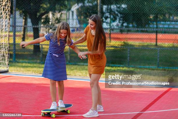 young mother is having fun with her daughter while they riding a skateboard together. - mother and daughter riding on skateboard in park stock pictures, royalty-free photos & images