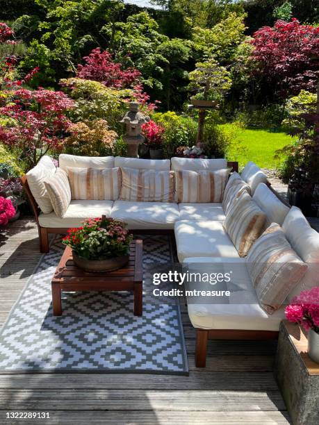 immagine di area relax all'aperto su soleggiata terrazza da giardino estiva con tappeto esterno, scanalato, ponte in legno imbiancato, posti a sedere in legno con cuscini, bonsai, maples giapponesi, giardino di design orientale paesaggistico, focus sul pri - arredamento da giardino foto e immagini stock