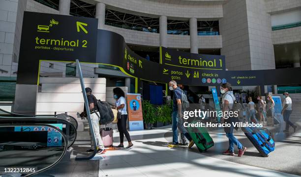 Mask-clad travelers push a luggage cart in Humberto Delgado International Airport a day before the country is taken off the UK's green list, imposing...