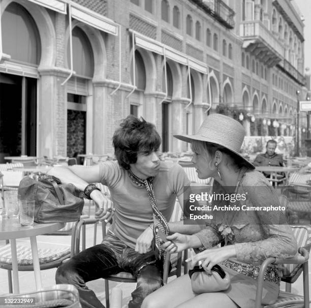 English musician Keith Richards talking to Anita Pallenberg, sitting outside the Excelsior Hotel, Lido, Venice, 1967.