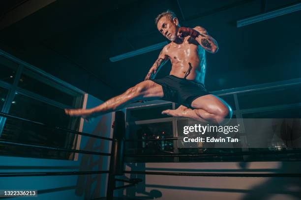 asian chinese senior man jump kick in gym boxing ring at night - kickboxing stock pictures, royalty-free photos & images