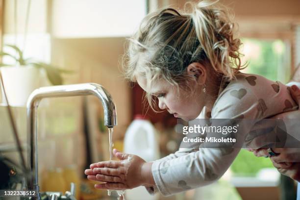 ontsproten van een vader die zijn kleine dochter helpt haar handen thuis wast - child washing hands stockfoto's en -beelden