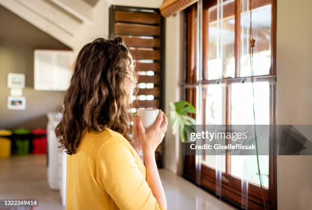 young woman drinking coffee while looking out her kitchen window - sunny morning stock pictures, royalty-free photos & images