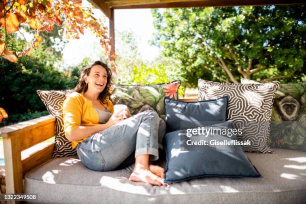 giovane donna che ride mentre si rilassa fuori nel suo patio con un caffè - woman home sit foto e immagini stock