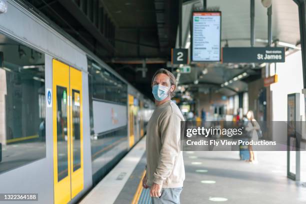 male wearing face mask waits on platform to board train - covid commuter stock pictures, royalty-free photos & images