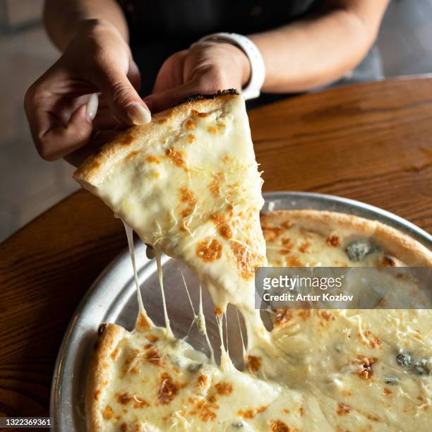 melted cheese pizza. woman taking large slice of hot pizza with stretching mozzarella cheese and appetizing golden brown crust. close up shot. italian food, junk food concept. soft focus - melted cheese stock pictures, royalty-free photos & images