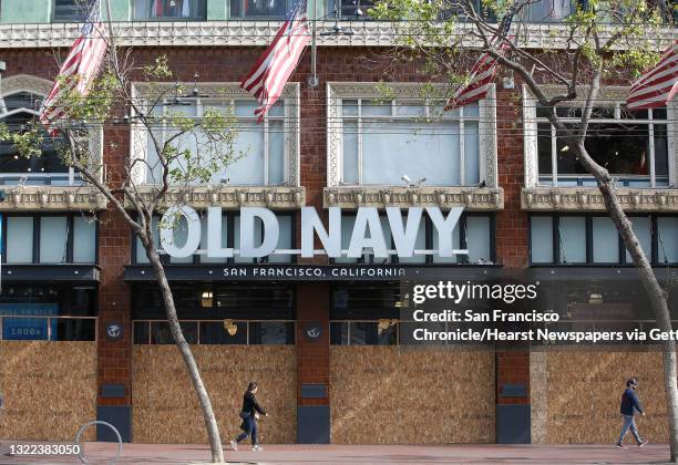 Pedestrians walk past a boarded up Old Navy store on Market Street on Friday, March 27, 2020 in San Francisco, Calif.