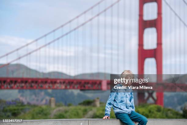 usa, ca, san francisco, boy sitting on wall near golden gate bridge - golden gate foto e immagini stock