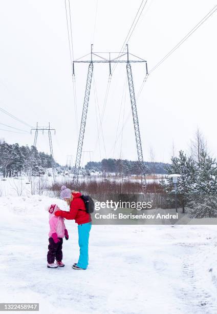 eine kaukasische familie, eine 40-jährige frau und eine tochter von 5 jahren, auf einem winterspaziergang. elektrische übertragungsleitung an der küste der bucht im winter. - 40 44 years woman stock-fotos und bilder