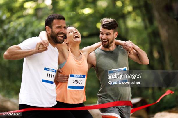 männliche läufer tragen erschöpfte athleten während des marathons bei sonnenuntergang. - marathon ziel stock-fotos und bilder