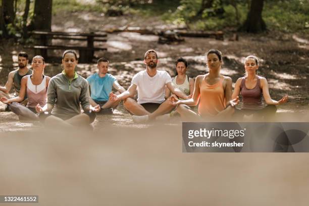 large group of athletes having yoga class in nature. - sitting eyes closed stock pictures, royalty-free photos & images