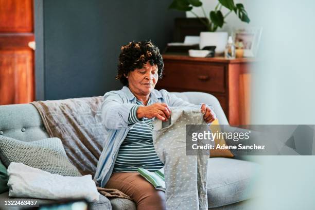 foto de una mujer mayor doblando la ropa recién lavada en el sofá de casa - folding fotografías e imágenes de stock