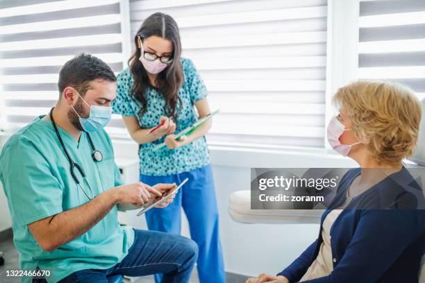 doctor looking at patient's medical record on digital tablet, nurse taking notes - doctor with male patient reading notes stock pictures, royalty-free photos & images