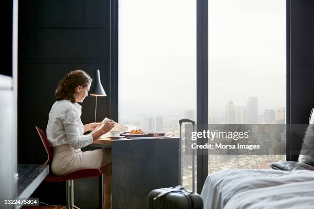 businesswoman reading newspaper at desk in hotel room - businesswoman hotel stock pictures, royalty-free photos & images