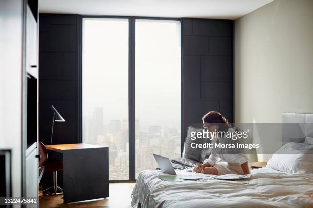 businesswoman using laptop on bed in hotel room - barcelona hotel stockfoto's en -beelden