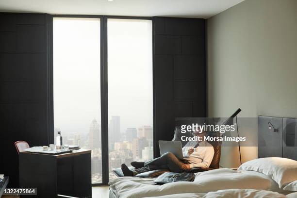 businessman using laptop while relaxing in hotel room - virtual meeting room stock pictures, royalty-free photos & images