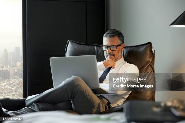thoughtful businessman using laptop in hotel room - businessman contemplation stockfoto's en -beelden