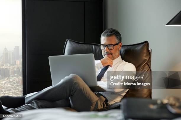 thoughtful businessman using laptop in hotel room - executivos imagens e fotografias de stock