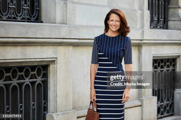 smiling businesswoman standing outside hotel - fashion business stockfoto's en -beelden