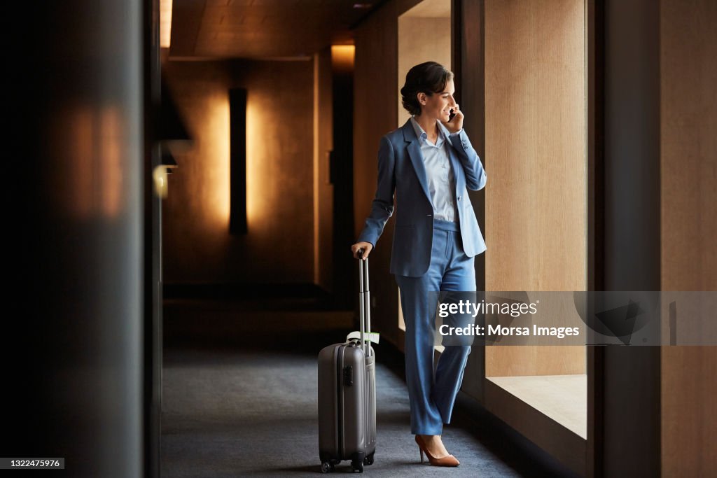 Businesswoman with luggage talking on smart phone