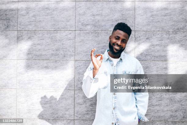 portrait of smiling young african man making ok gesture against gray background. - ok zeichen stock-fotos und bilder