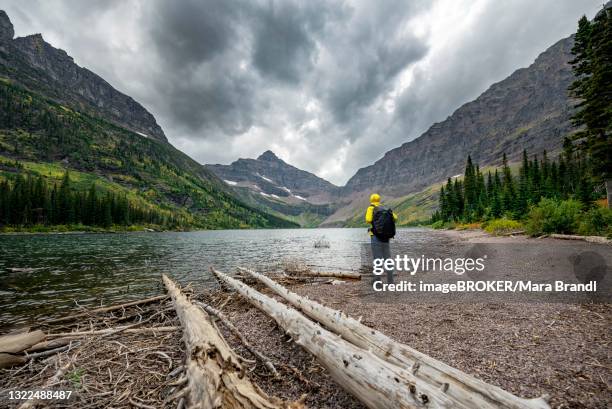 hikers at upper two medicine lake, mountain peaks lone walker mountain and mount rockwell in the background, dramatic clouds, glacier national park, montana, usa - two medicine lake montana stock-fotos und bilder