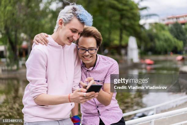 two smiling men looking at a smart phone - non binary stereotypes stock pictures, royalty-free photos & images