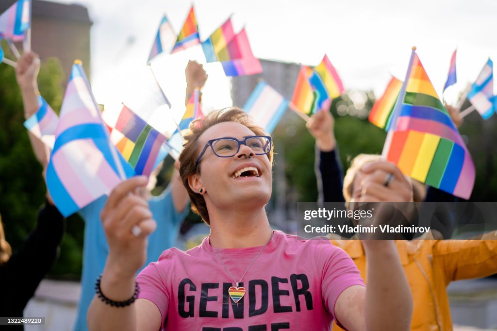 LGBTQ+ Aktivist hält Regenbogenfahnen in den Händen und blickt in den Himmel