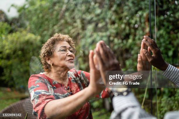 senior couple separated greeting through the window at home - covid separation stock pictures, royalty-free photos & images