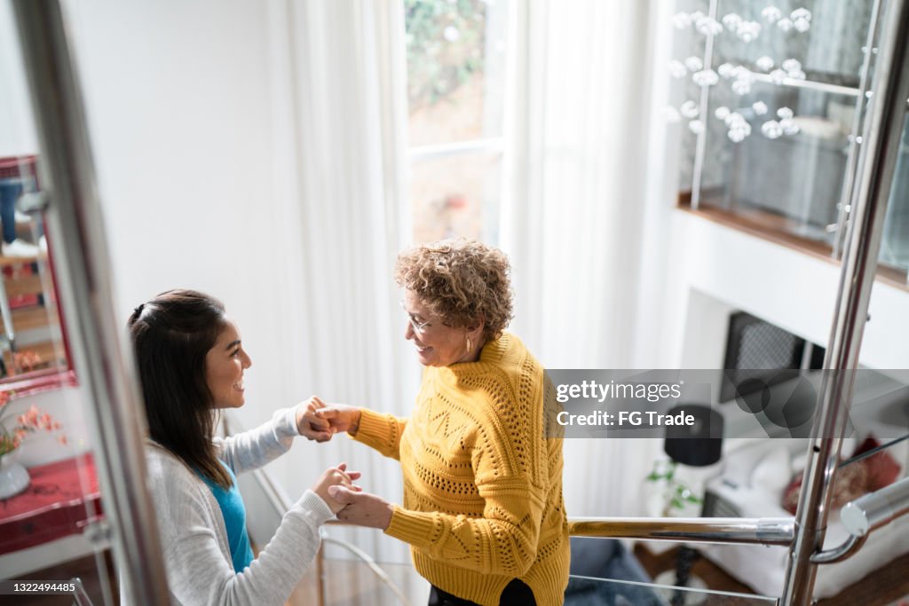 Nurse supporting senior patient walking or moving up the stairs at home