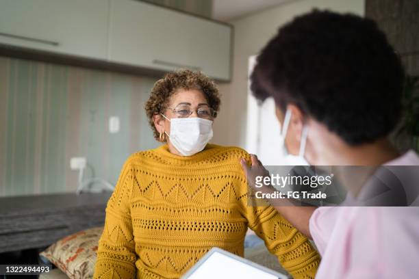 arzt consoling senior patient zu hause - tragen gesichtsmaske - african mask stock-fotos und bilder