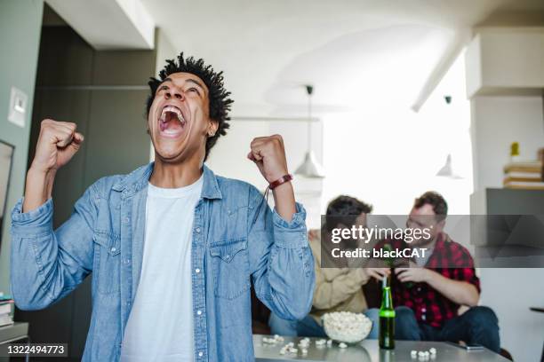 grupo emocionado de amigos varones viendo deportes en casa - apuestas deportivas fotografías e imágenes de stock