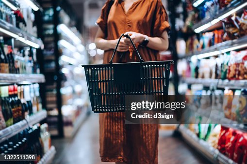 Cropped shot of young woman carrying a shopping basket, standing along the product aisle, grocery shopping for daily necessities in supermarket Cropped shot of young woman carrying a shopping basket, standing along the product aisle, grocery shopping for daily necessities in supermarket