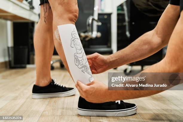 unrecognizable tattoo artist placing the paper stencil with the tattoo design on the client's leg. - animal leg stockfoto's en -beelden