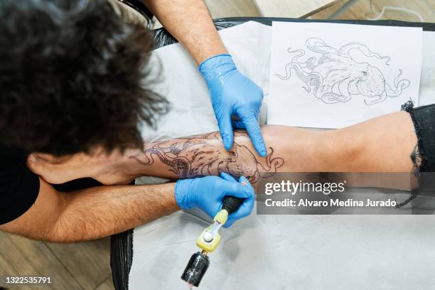 top view of an unrecognizable tattoo artist tattooing an octopus design on his client's leg. - tatuaje fotografías e imágenes de stock