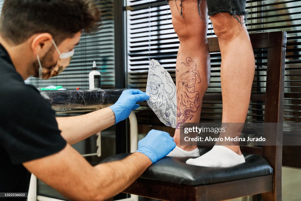 Tattooist Removing The Paper Stencil With The Tattoo Design On The Clients Leg To Check That It Has Been Drawn On The Clients Skin High-Res Stock Photo - Getty Images Tattooist Removing The Paper Stencil With The Tattoo Design On The Clients Leg To Check That It Has Been Drawn On The Clients Skin High-Res Stock Photo - Getty Images