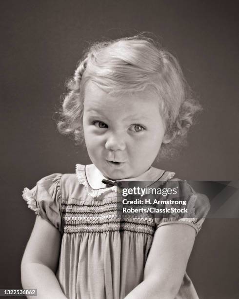 1930s 1940s Blond Toddler Girl Looking At Camera Up And To The Side Shy Bashful Facial Expression Wearing Dress With Smocking.