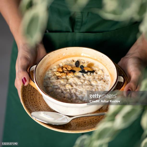 traditional english breakfast. woman holds bowl of cereal oatmeal or porridge with milk, raisins and nuts. close up shot. soft focus - fiocchi di avena foto e immagini stock