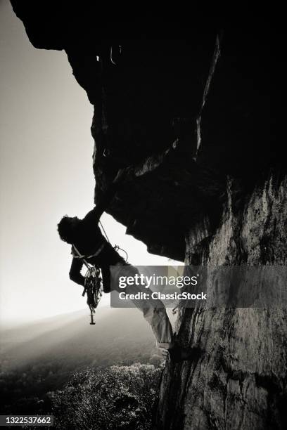 1980s Anonymous Silhouetted Rock Climber Hanging From Rock Sunlight Over Smaller Mountains In B/G Shwanagunk Mountains ny USA.