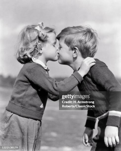 1930s 1940s Serious Little Girl Kissing Smiling Little Boy Both Outdoors Wearing Knit Wool Sweaters.
