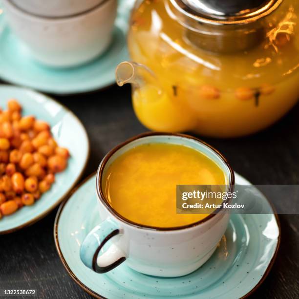 full cup of orange sea buckthorn tea, close-up shot. vitamin healthy drink useful for strengthening immune system. fresh berries and glass teapot with healing drink on blurred background. soft focus - buckthorn stock pictures, royalty-free photos & images