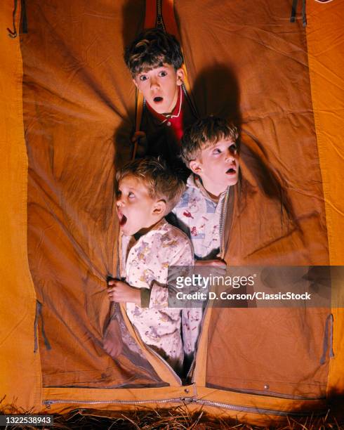 1960s Camping Adventure Three Scared Frightened Boys Brothers Looking Out Of Tent Flap Opening At Night One Looking At Camera .