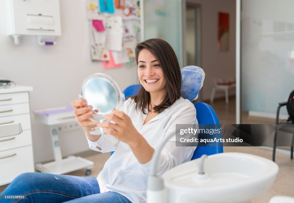 Jonge Vrouw die Spiegel met Glimlach in het Bureau van de Tandarts bekijkt