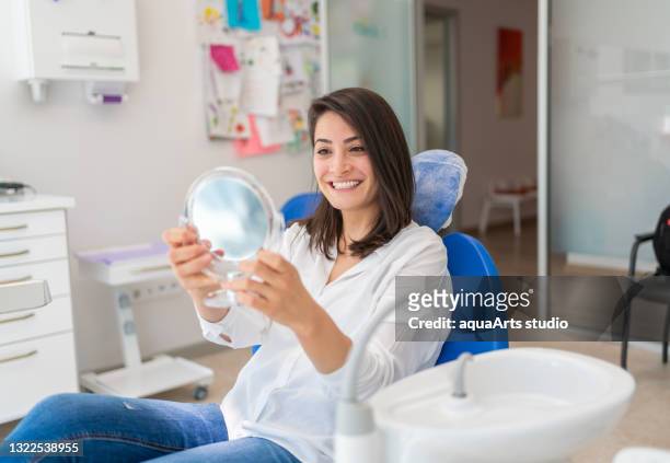 young woman looking at mirror with smile in dentist’s office - consultório dentário imagens e fotografias de stock