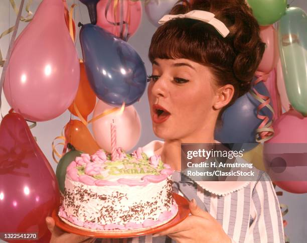 1960s Woman Blowing Out Single Candle On Birthday Party Cake .