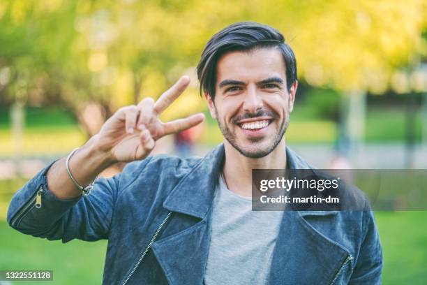 lächelnder mann zeigt das friedenszeichen - victory sign stock-fotos und bilder