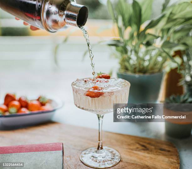 cocktail being poured from a metal cocktail shaker into a stylish glass - drink stock pictures, royalty-free photos & images