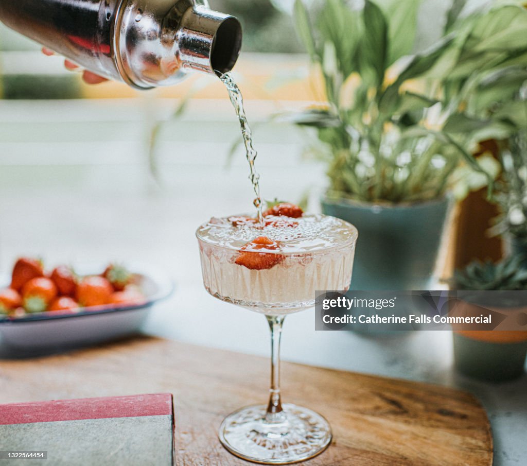 Cocktail being poured from a metal cocktail shaker into a stylish glass