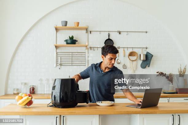 mann mit luftfritteuse und laptop in der küche - airfryer stock-fotos und bilder