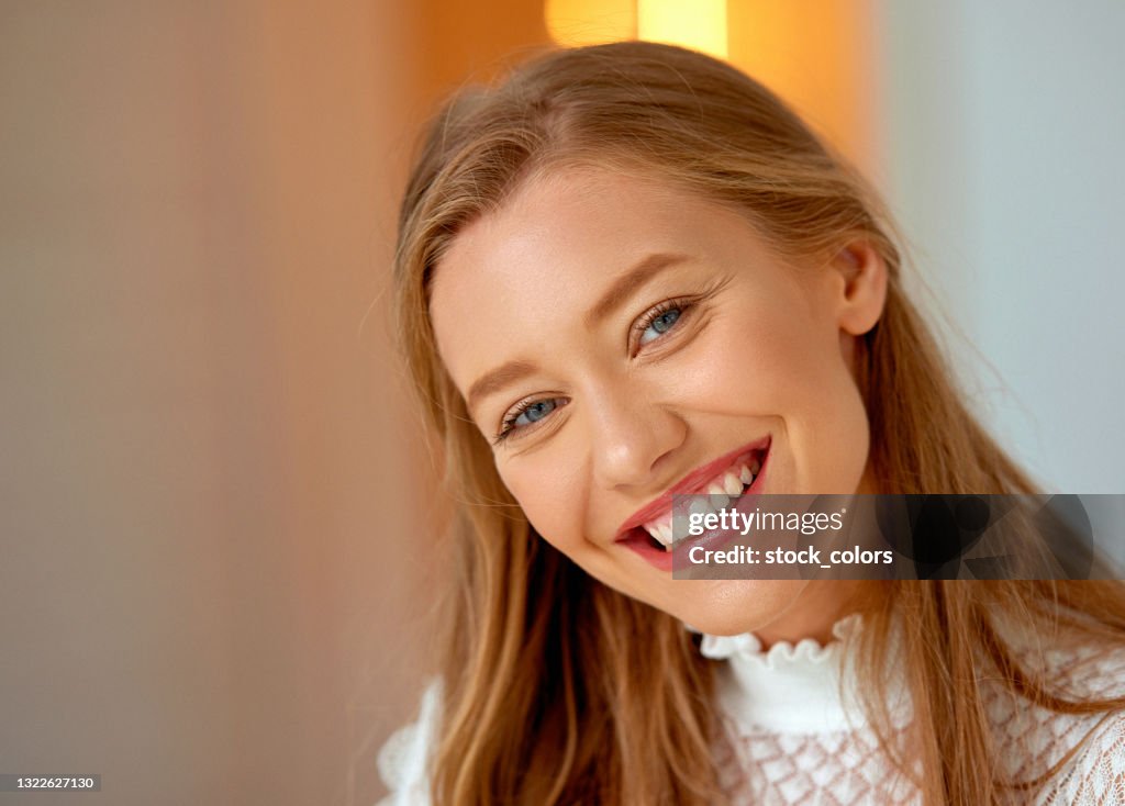 Beautiful blond woman with toothy smile looking at camera indoors